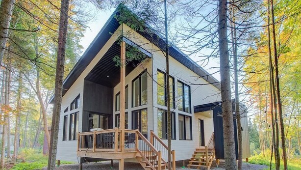Une cabane dotée d’une terrasse, de grandes fenêtres et située en pleine forêt.