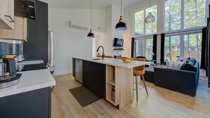 Une cuisine moderne dotée d’un îlot central, de luminaires suspendus et de grandes fenêtres.
