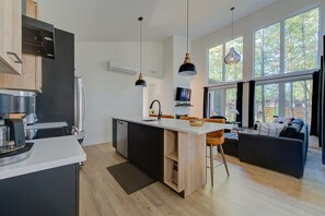 Eine moderne Küche mit einer zentralen Kochinsel, Pendelleuchten und großen Fenstern.