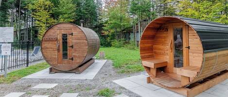 Two wooden sauna cabins with a metal roof, surrounded by a forested area.