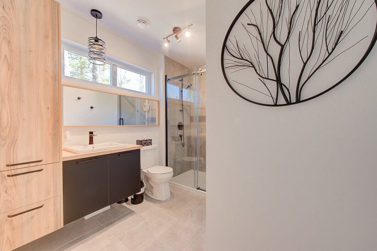 Een moderne badkamer met een houten wastafelmeubel, een douchecabine van glas en een kunstwerk aan de muur.
