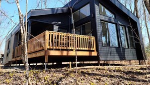 A modern cabin with a wooden deck, large windows, and a dark exterior.