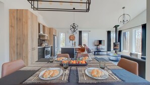 A modern dining area with a table set for two, a kitchen in the background, and a fireplace.