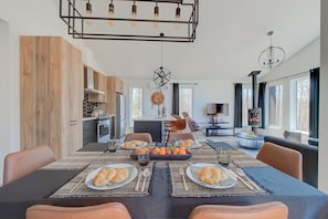 A modern dining area with a table set for two, a kitchen in the background, and a fireplace. - Le Cerf Blanc | Nature & EV Charger (Pont-Rouge)