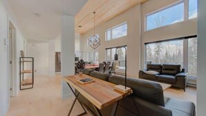 Un salon moderne avec une table à manger en bois, un canapé et de grandes fenêtres donnant sur l’extérieur.
