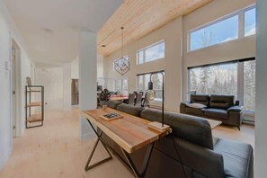 Una sala de estar moderna con una mesa de comedor de madera, un sofá y amplias ventanas que ofrecen vistas al exterior.