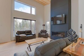 Una sala de estar moderna con chimenea, sofás de cuero, una mesa de centro y ventanas amplias.