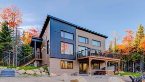 Une maison moderne à deux étages, dotée d’un balcon, d’une terrasse et d’un chemin en pierre menant à l’entrée.