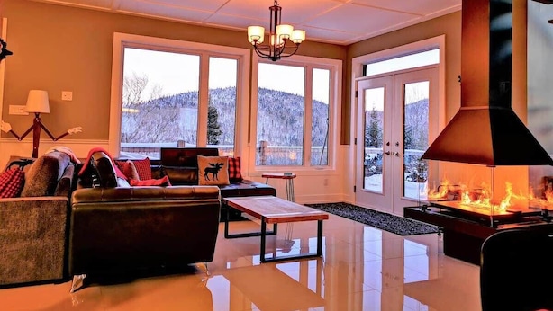 A spacious living room with a fireplace, large windows, and a chandelier. - Pourquoi Pas! - Hot tub and Ski, Mountain view (Saint-Philémon)