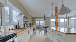 A modern kitchen with a large island, pendant lighting, and a view through the glass door. - Pourquoi Pas! - Hot tub and Ski, Mountain view (Saint-Philémon)