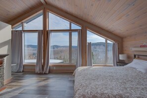 A bedroom with a large skylight, a bed, a stone fireplace, and a view of the outdoors.