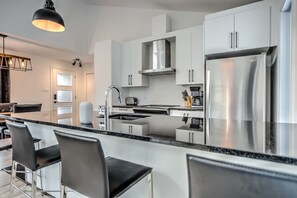 Une cuisine moderne avec des meubles blancs, des appareils en acier inoxydable et un îlot central doté de tabourets de bar.