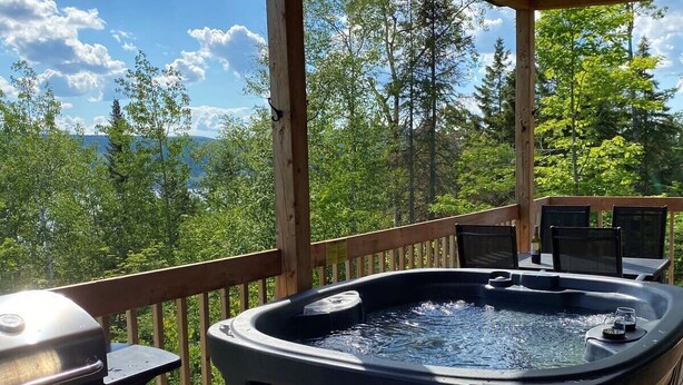 A hot tub on a wooden deck with a view of a forest and mountains. - L'Enchanteur - Hot tub and Pet friendly (Pohénégamook)