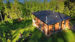 A modern house with a flat roof, surrounded by a lush green landscape and a lake. - L'Enchanteur - Hot tub and Pet friendly (Pohénégamook)