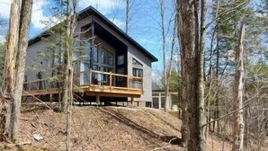 A modern two-story cabin with a balcony, surrounded by trees.