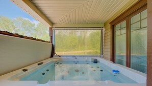 Un jacuzzi con vistas a un bosque, un porche cubierto y una ventana con persianas.