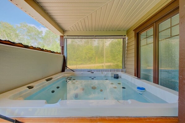 A hot tub with a view of a forest, a covered patio, and a window with blinds. - L'Escapade - Spa, billard & foyer (Petite-Rivière-Saint-François)