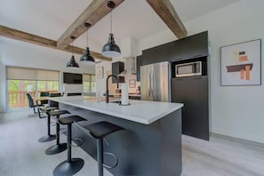 Una cocina moderna con una isla grande, taburetes de bar, iluminación colgante y un refrigerador de acero inoxidable.