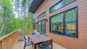 A wooden deck with a table and chairs, large windows, and a view of a forest. - L'Escapade du Domaine - Peaceful Nature Stay (Pont-Rouge)