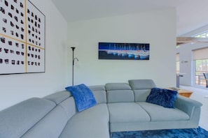 Una sala de estar moderna con un sofá seccional gris, un cuadro con barcos y una lámpara de pie.