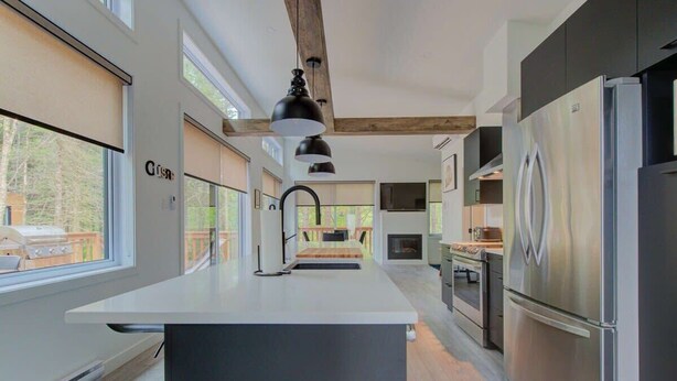 A modern kitchen with a central island, stainless steel appliances, and large windows. - L'Escapade du Domaine - Peaceful Nature Stay (Pont-Rouge)
