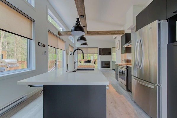 A modern kitchen with a central island, stainless steel appliances, and large windows.