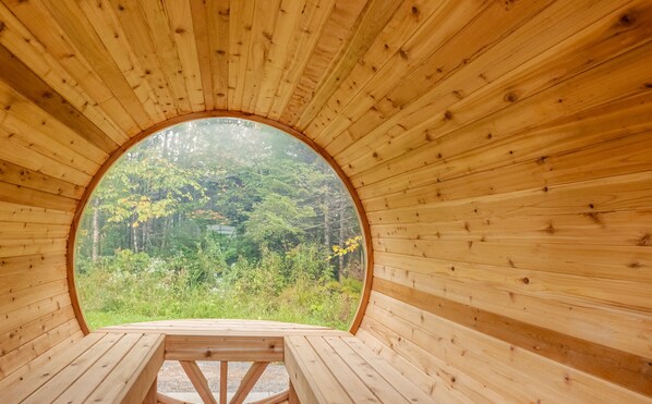 Relax in a cozy cabin surrounded by a lush forest, with a circular window offering a serene view.