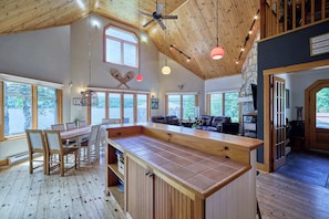 A spacious kitchen with a wooden island, large windows, and a dining area with chairs and a table. - Grand Chene - Private Spa & Lakefront (Pohénégamook)