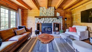 A log cabin interior with a stone fireplace, wooden ceiling beams, a sofa, a coffee table, and a television. - Grandes-Piles | Spa, dock, navigable river & ski (Grandes-Piles)