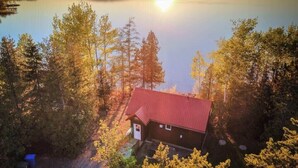 A cabin with a red roof surrounded by trees, overlooking a calm lake. - Le Huard - Lakefront & Private Dock (Sayabec)
