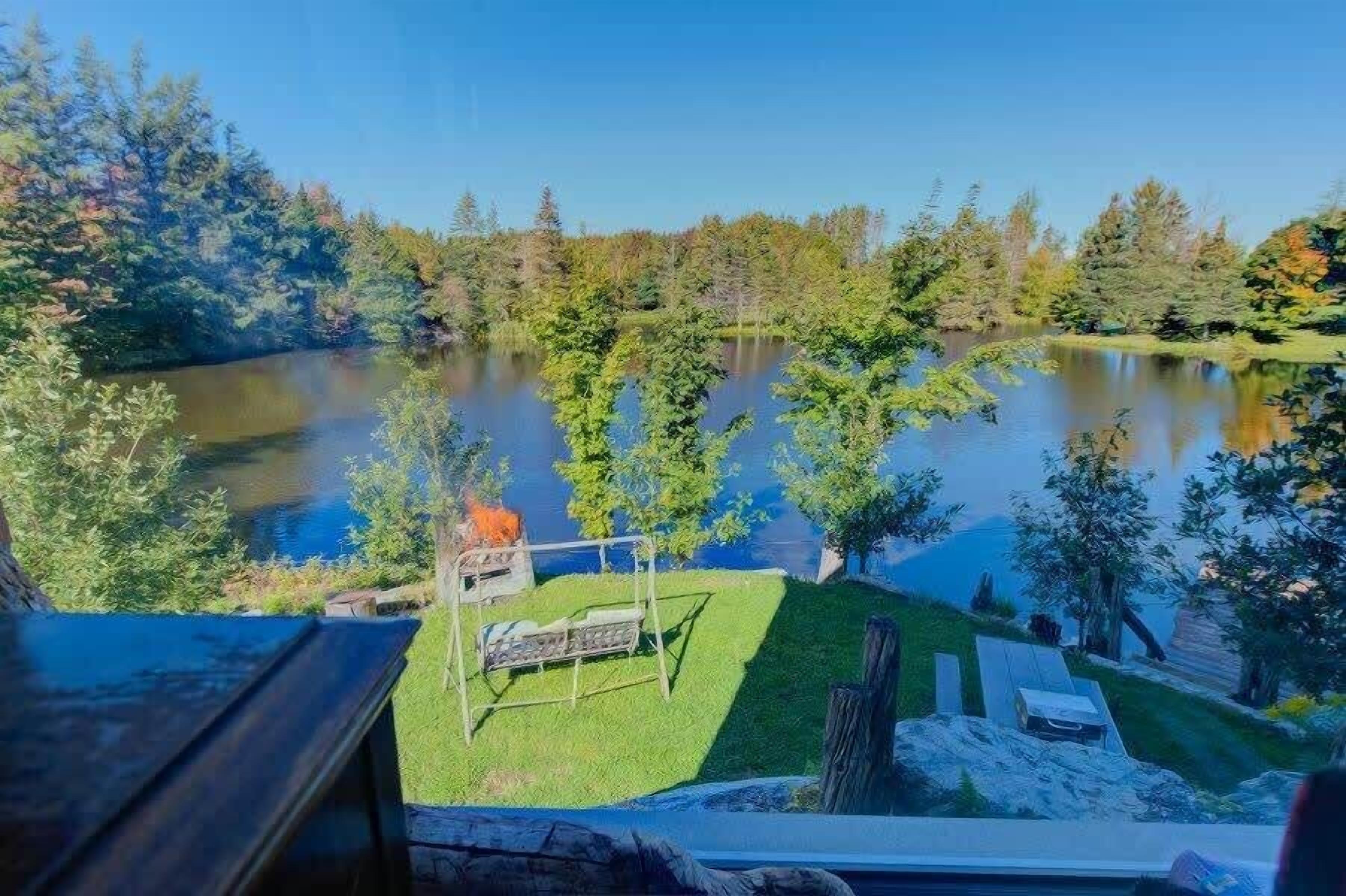 A lakeside view with a grassy area, a swing set, and a wooden deck.