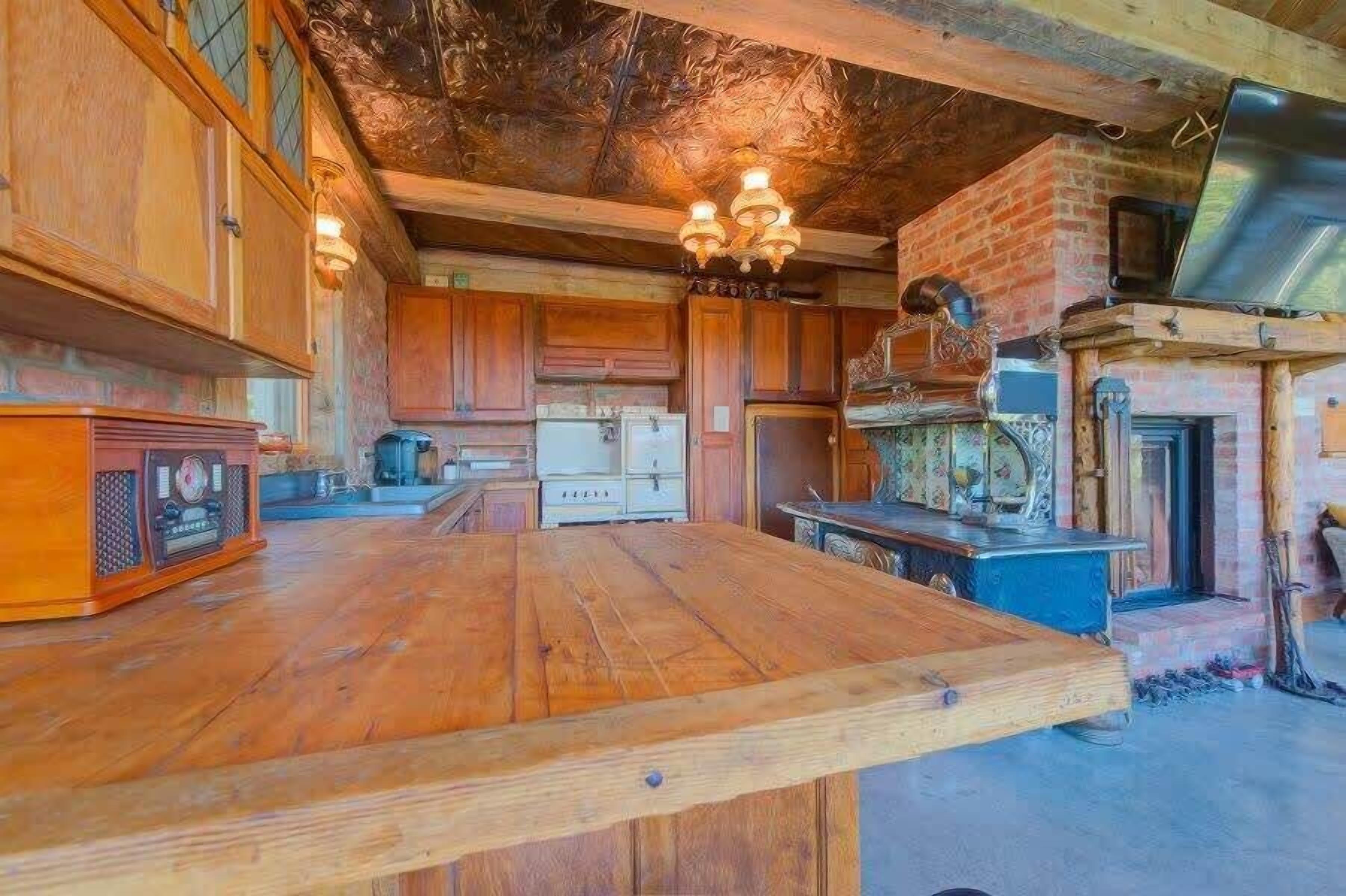 A rustic kitchen with wooden cabinets, a large wooden table, and a brick fireplace.