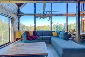 Et hyggeligt sommerhusinteriør med et stort vindue, et træbord, en sofa og en loftsvifte.