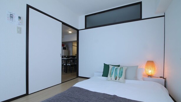 A modern hotel room with a large bed, a bedside lamp, and a view of the dining area.
