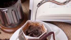 A coffee cup with a heart-shaped handle and a paper filter, with coffee being poured into it.