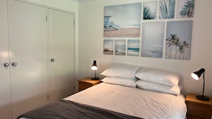 Une chambre à coucher avec un lit, deux tables de chevet, une commode et une porte.