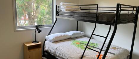 A bunk bed with a window view, a bedside table, and a lamp.