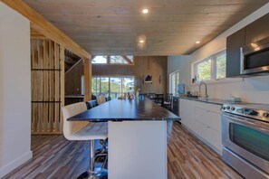 A modern kitchen with a central island, wooden flooring, and large windows.
