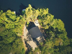 An aerial view of a cabin surrounded by dense forest, with a clear path leading to the entrance.