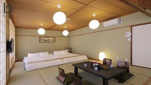 Ein traditioneller japanischer Raum mit Tatami-Bodenbelag, einem niedrigen Tisch mit Kissen und einem Bett mit weißer Bettwäsche.