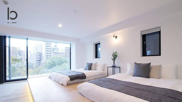Une chambre d’hôtel moderne avec deux lits, une grande fenêtre donnant sur la ville et une petite table agrémentée d’une plante.