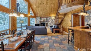 Un amplio salón con chimenea de piedra, piso de madera y un gran ventanal con vistas a un paisaje nevado.