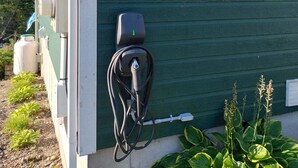 Una casa con un cartel que anuncia 'CHALETS Confort' y una estación de carga para vehículos eléctricos.