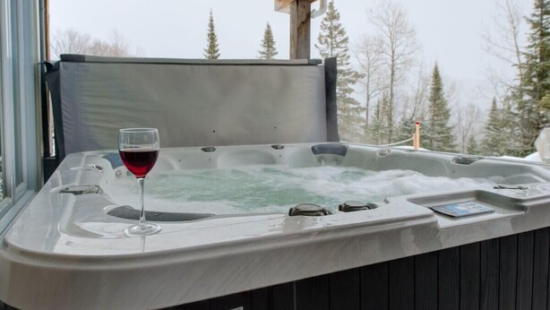 Un jacuzzi con una copa de vino tinto, rodeado por una terraza de madera y vistas a árboles.