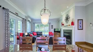 A spacious living room with a glass dining table, a fireplace, and a large window.