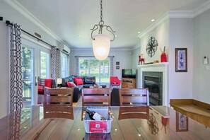 A spacious living room with a glass dining table, a fireplace, and a large window.
