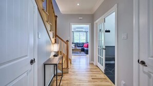 A hallway with a wooden staircase, a console table, and a view into a living area with a sofa and a window. - La Nouvelle-Angleterre - Hot tub and Dock (Pohénégamook)