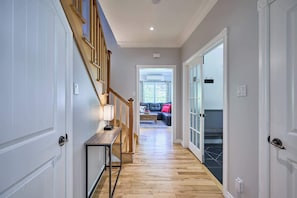 A hallway with a wooden staircase, a console table, and a view into a living area with a sofa and a window.