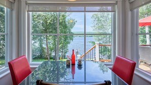 A dining table with chairs, a bottle, and a cup, with a view of a lake and trees through large windows. - La Nouvelle-Angleterre - Hot tub and Dock (Pohénégamook)