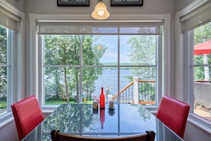 A dining table with chairs, a bottle, and a cup, with a view of a lake and trees through large windows.